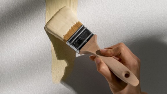 Seinää maalaava käsi, tela ja keltainen maali