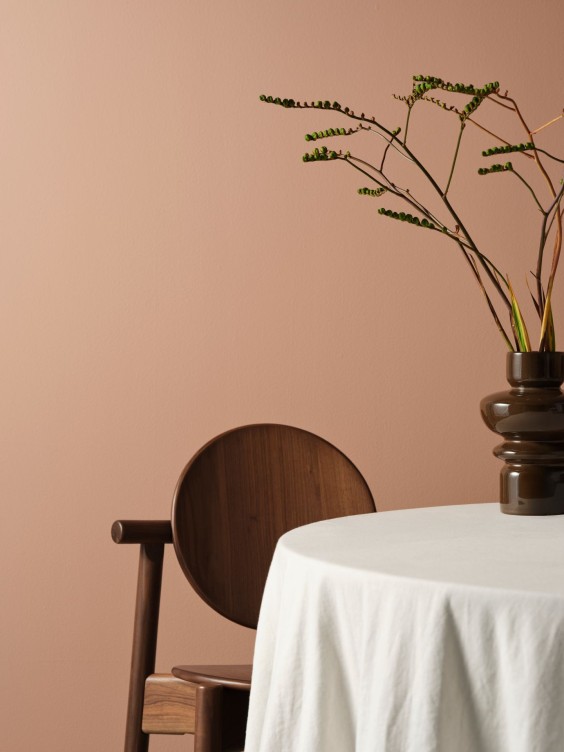 Romara-sävy seinällä. Pöytä, jossa valkoinen pöytäliina ja pähkinänruskea tuoli.