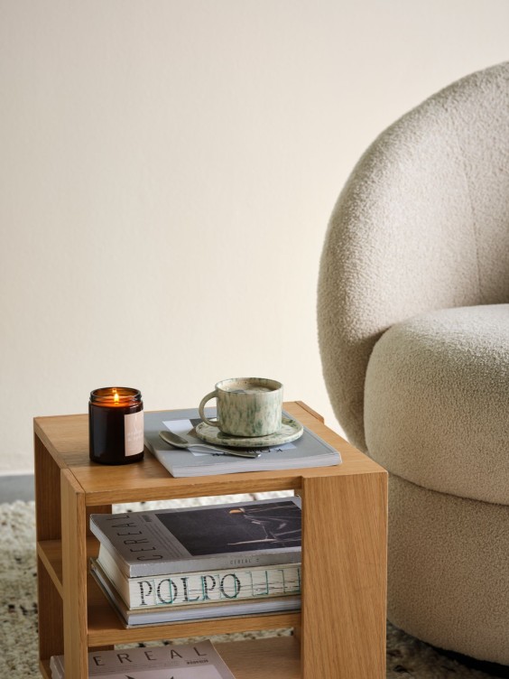 Velmira-sävy seinällä. Edessä vaalean nojatuolin kulma ja pieni sohvapöytä.