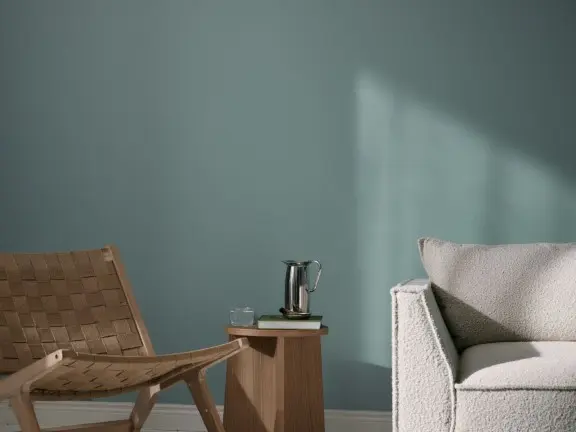 Rauhallinen olohuone, jossa seinällä Mute syvämattamaali. Edessä vaalea sohva, tuoli ja pieni sivupöytä.
