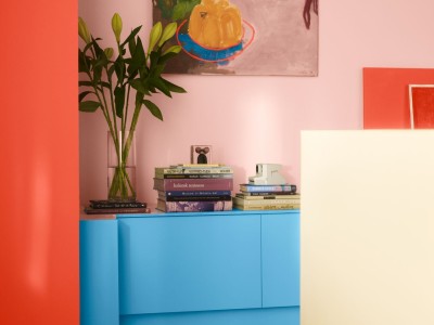 Punaista seinillä, sinistä lipastossa ja keltainen pöytä. Seinällä näyttävä maalaus. 