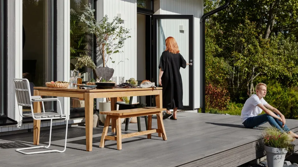 Nainen astumassa sisään valkoiseen puutaloon ja poika istumassa sen edessä terassilla