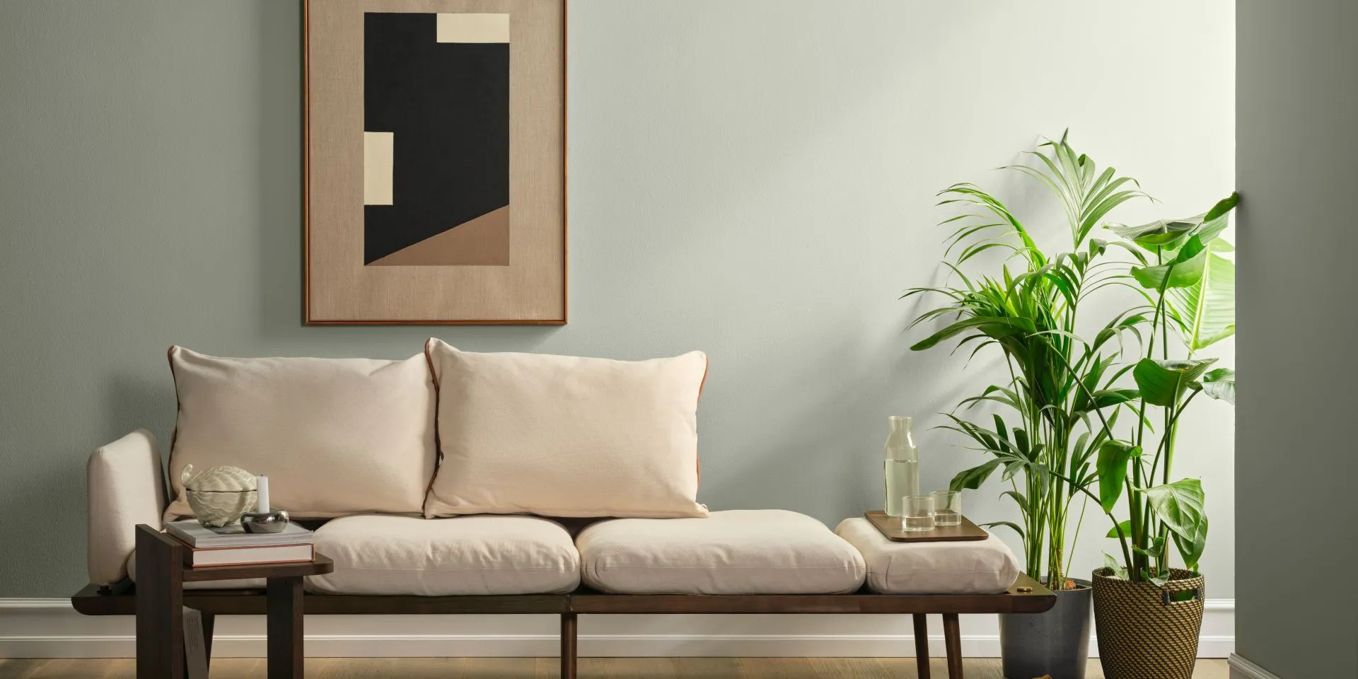 Thalora-sävy seinällä. Edessä penkki, huonekasvi ja pieni pöytä. Seinällä graafinen taideteos.