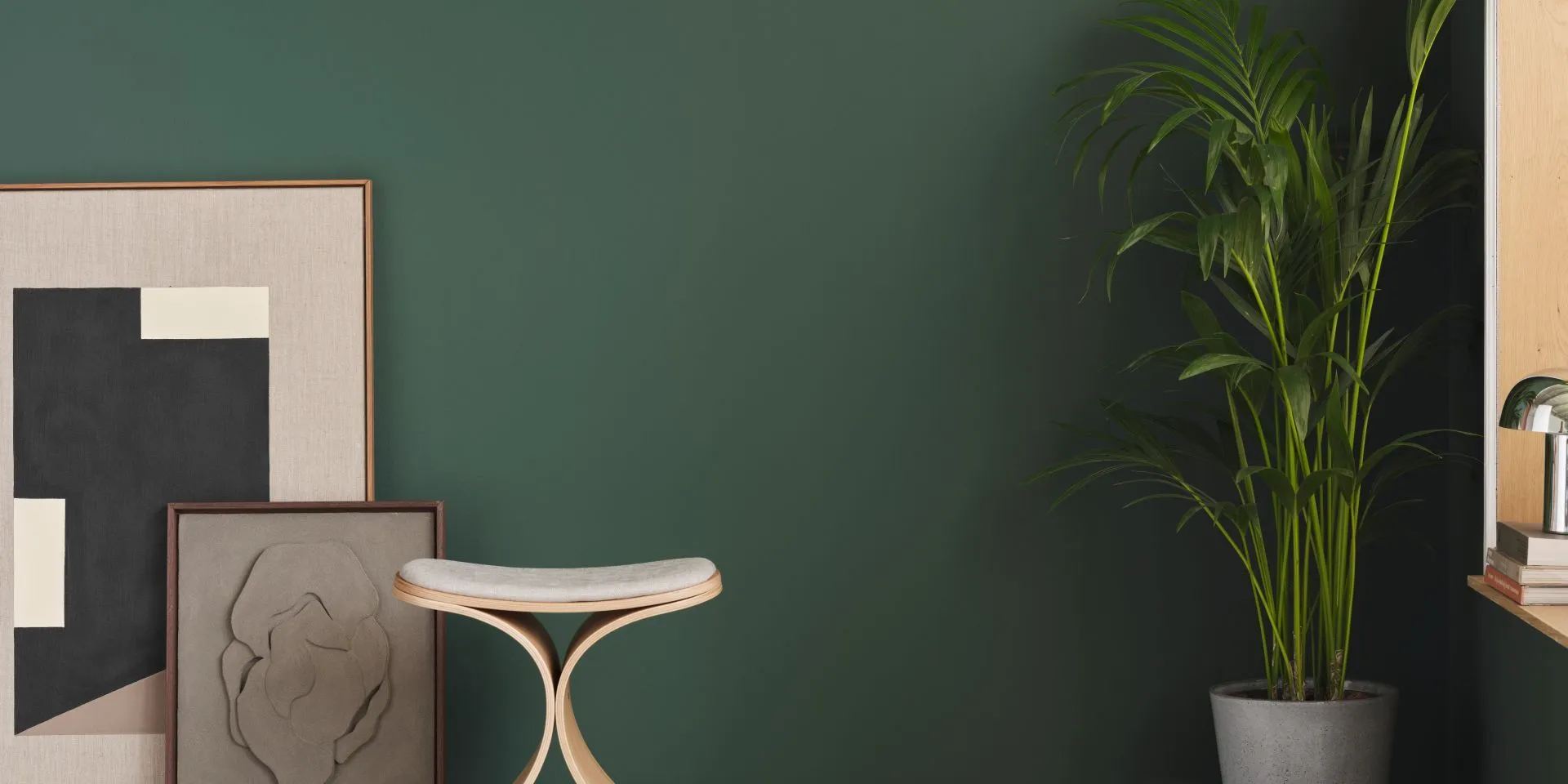 Seinällä metsänvihreä, syvämatta Mute Veradalis. Edessä huonekasvi ja taidetta.