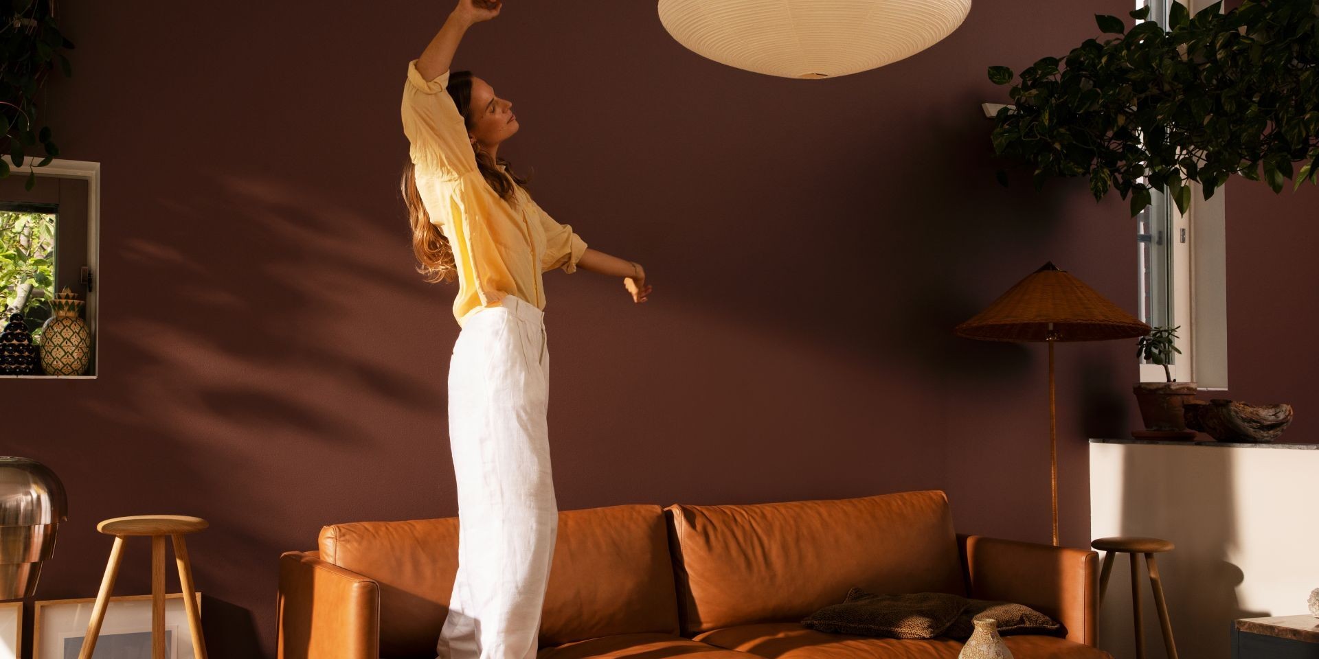 Nainen tanssimassa viihtyisässä olohuoneessa, jossa lämpimän ruskean värinen seinä ja sovha