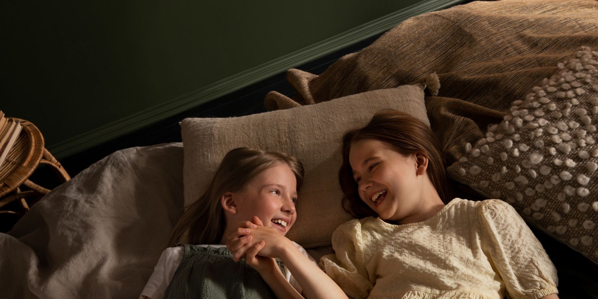 Kaksi tyttöä makaamassa sängyssä tumman sävyisessä huoneessa