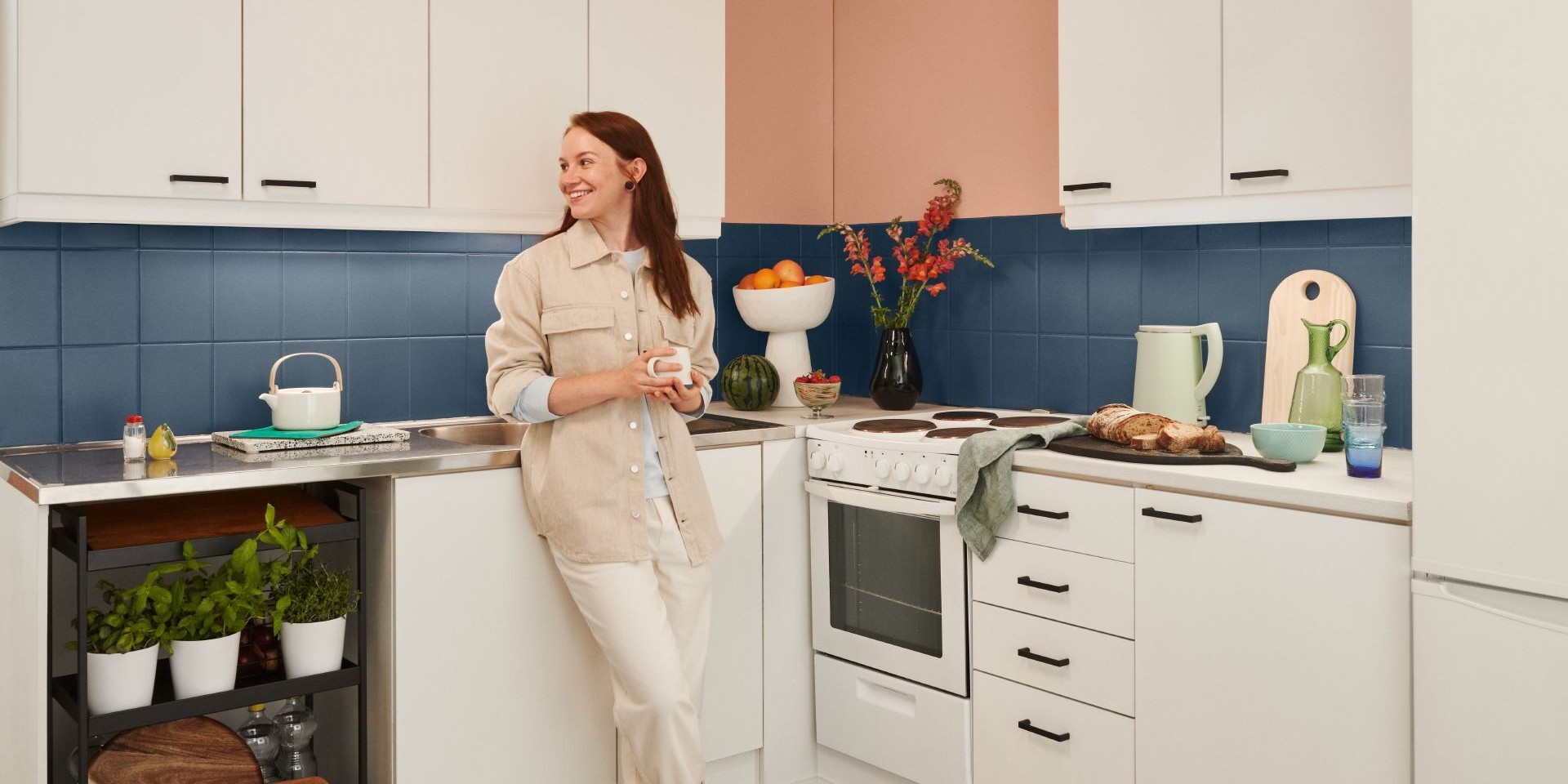 Nainen keittiössä, jossa on siniset kaakelit ja persikanvärinen seinä 