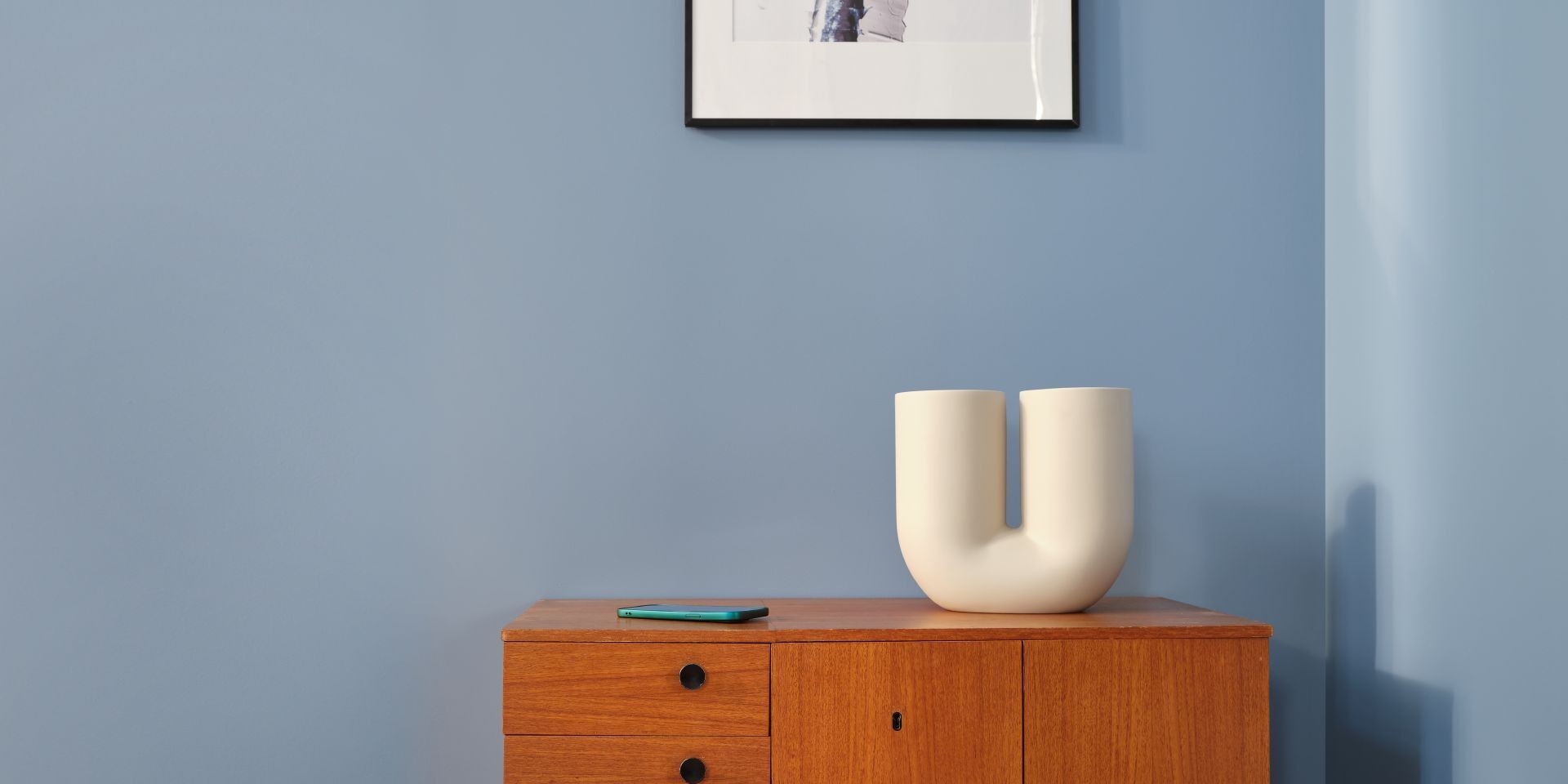Sininen seinä ripauksella harmaata olohuoneessa ja puinen lipasto