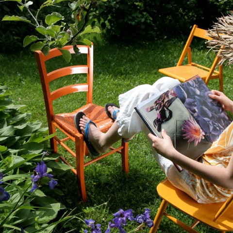 nainen lukemassa lehteä pihalla maalatulla puutuolilla