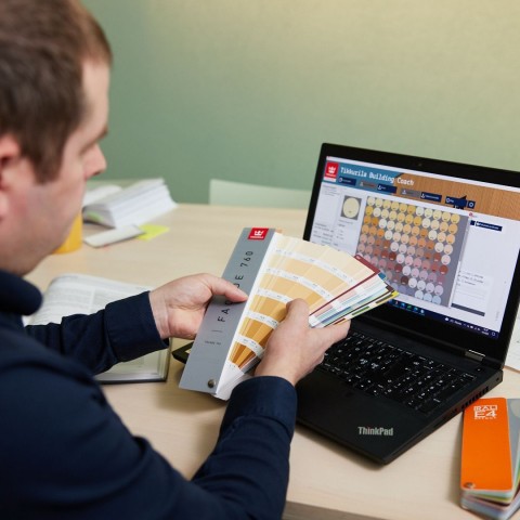 Suunnittelijalla Tikkurila Facade väriviuhka kädessä ja Building Coach ohjelmisto auki tietokoneella.