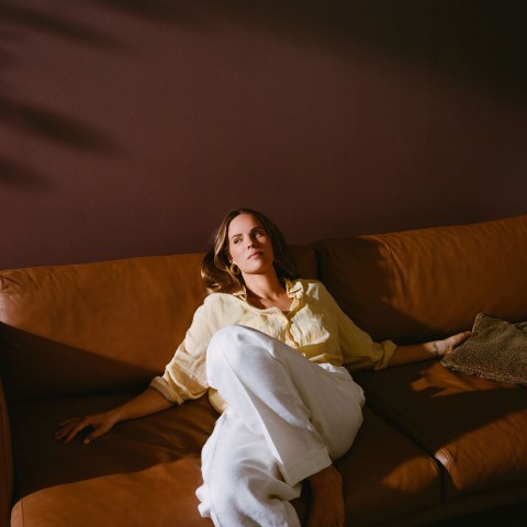 Nainen rentoutuu ruskealla nahkasohvalla ja lämpimän ruskea seinäväri taustalla