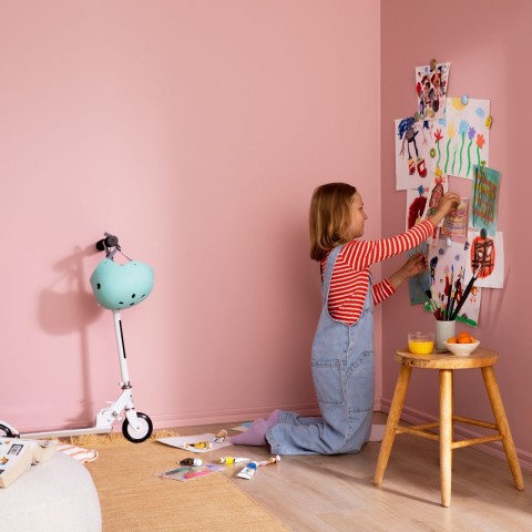 Lapsi asettamassa julisteita oman huoneen vaaleanpunaisille seinille