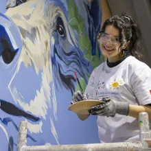 A woman smiling while painting a mural