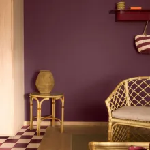 Olohuone, jossa luumunvioletti seinä ja rottinkinojatuoli.