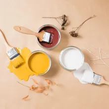 Kolme maalipurkkia ja pensselit beigellä alustalla