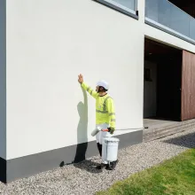 Maalari kivitalon ulkoseinän vieressä.