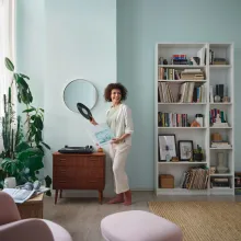 Nainen levysoittimen edessä vedenvihreässä olohuoneessa