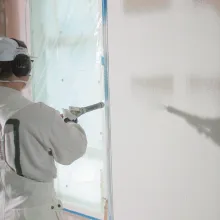 Maalari ruiskuttaa valmistasoitetta kipsiseinään.