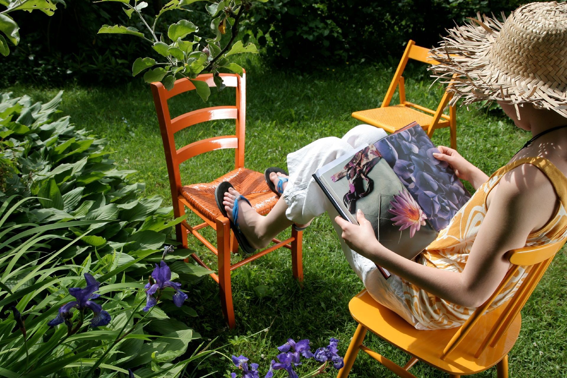 nainen lukemassa lehteä pihalla maalatulla puutuolilla