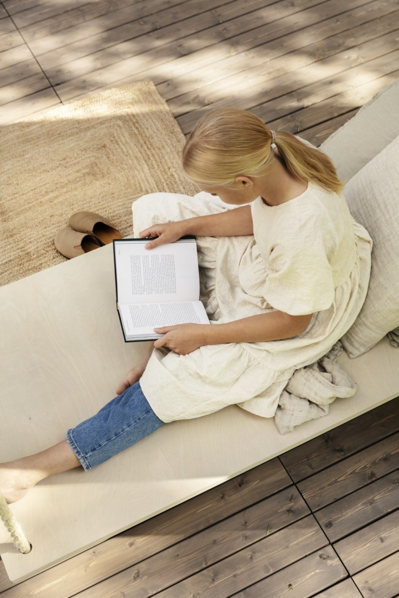 Vaalea tyttö lukee kirjaa terassilla daybedin päällä.