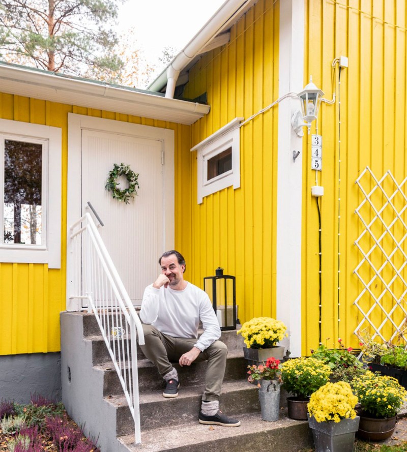 Mies istumassa keltaisen mökin edessä portailla