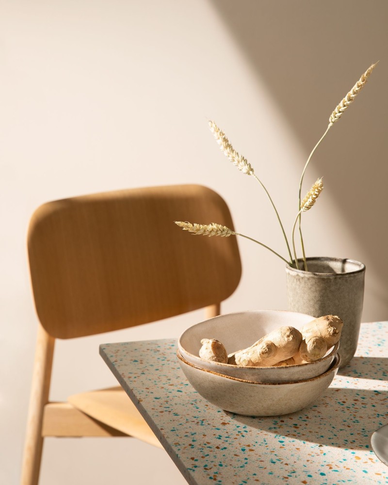 Beige seinä, puinen tuoli ja maanläheinen sävymaailma ruokapöydällä