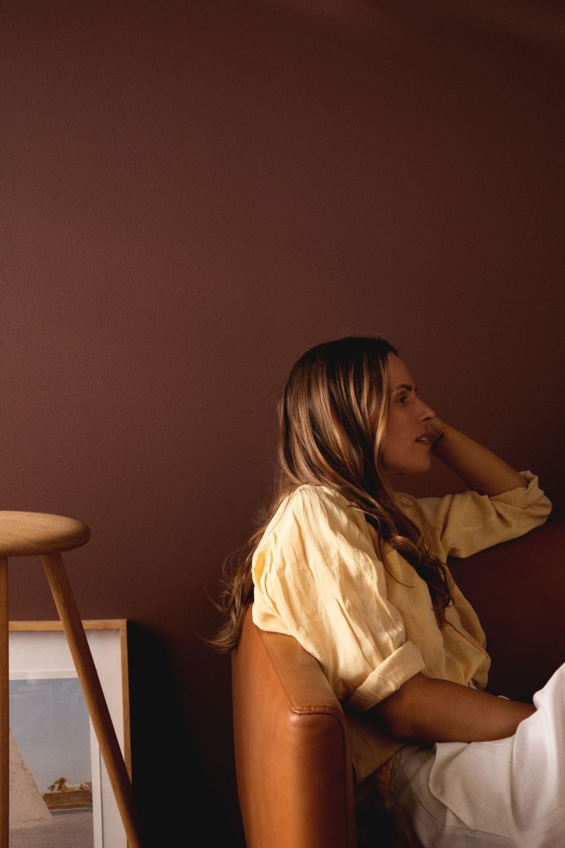 Nainen istuu sovhalla lämpimän ruskean seinän edessä