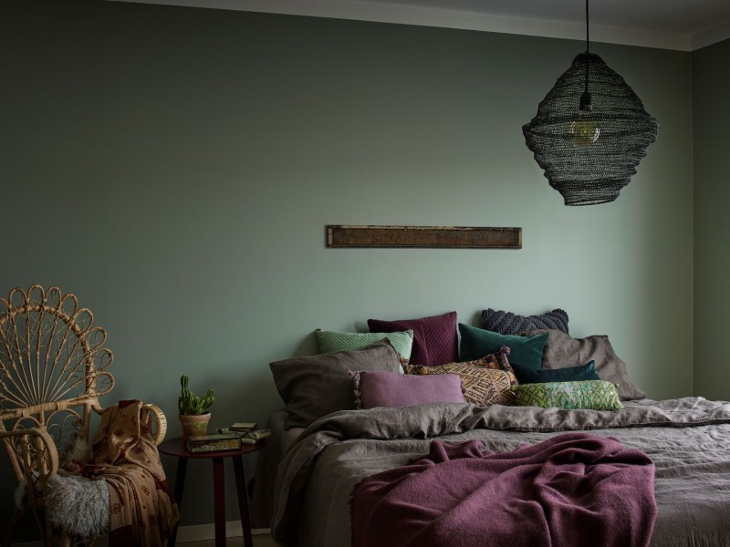 vihreä makuuhuoneen seinä boheemeilla tyynyillä ja lampulla