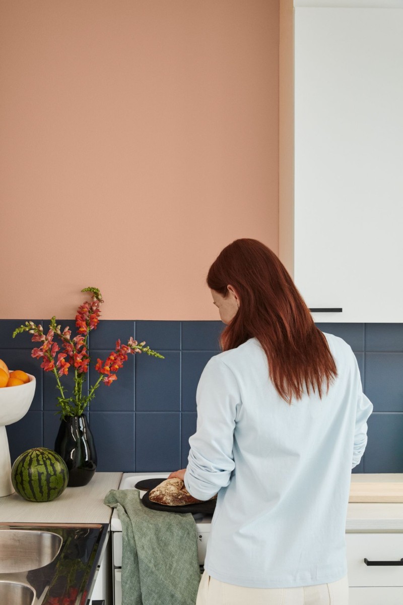 Nainen lämpimän persikansävyisen seinän ja siniseksi maalattujen kaakeleiden edessä