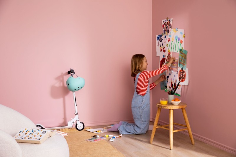 Lapsi ripustamassa piirrustuksia vaaleanpunaisen huoneen seinille