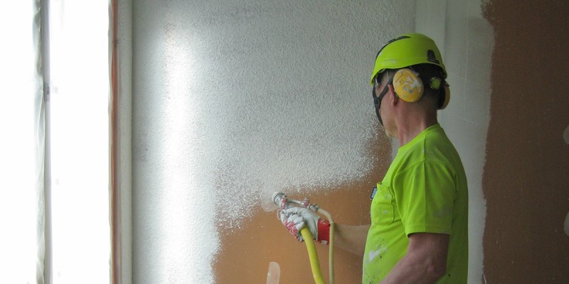 Työmies levittää ruiskutasoitetta seinään.